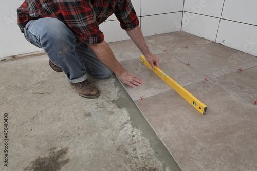 Worker using level tool to measure tiles position at floor, kitchen or bathroom renovation