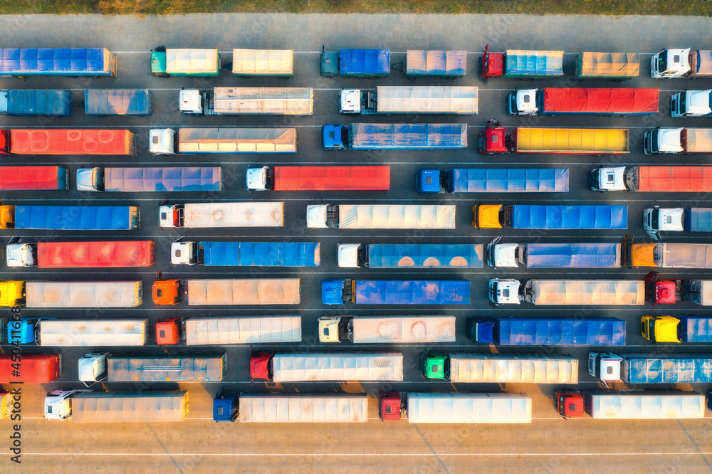 Aerial view of colorful trucks in terminal at sunset in summer. Top view of logistic center. Heavy industry. Transportation. Cargo transport, shipping. International trucking. View from drone of truck Aerial view of colorful trucks in terminal at sunset in summer. Top view of logistic center. Heavy industry. Transportation. Cargo transport, shipping. International trucking. View from drone of truck