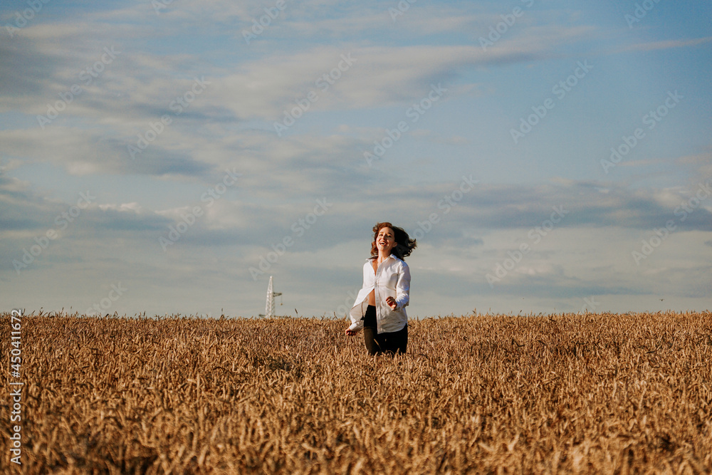 Happy woman in a white shirt runs in a wheat field on a summer day. Happiness and joy concept Happy woman in a white shirt runs in a wheat field on a summer day. Happiness and joy concept