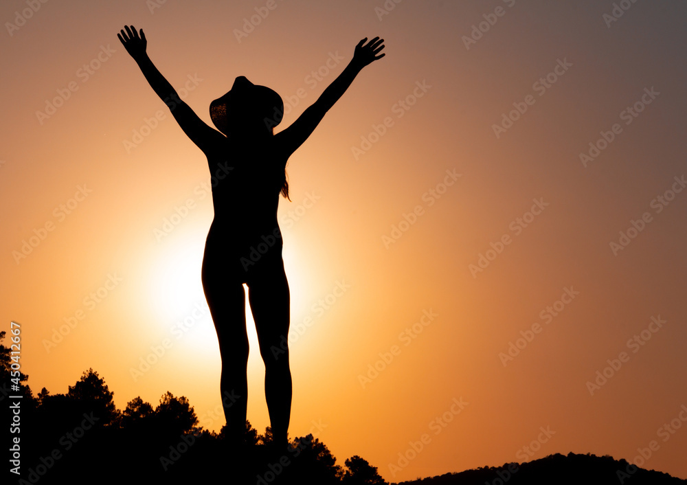 Silhouette of woman at sunset, facing the sun, wearing a hat. Concept of strength and overcoming. Selective focus.  Overcoming problems. Reaching a goal. Copy space. Self-confidence.