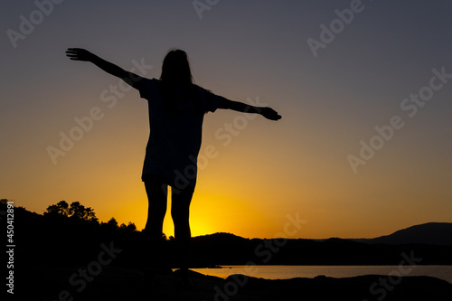 Silhouette of woman at sunset with outstretched arms. Overcoming life's difficulties. Concept of reflection and thought. Selective focus. Copy space. Reaching a goal. Self-confidence.