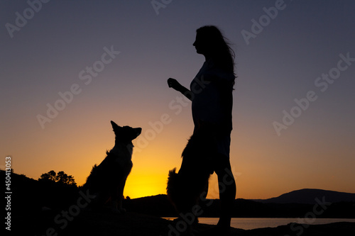 Silhouette of woman playing with a dog at sunset in front of a lake. Love for animals. Selective focus. Copy space.