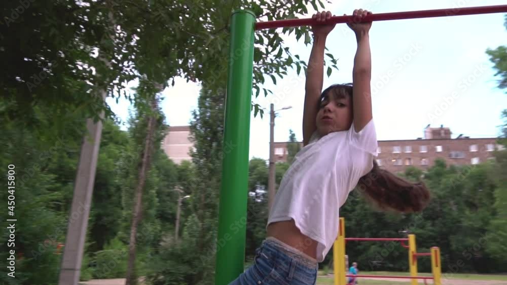 A teenage girl is engaged on horizontal bars. Playground. The child goes in for sports. City block. Leisure park. Workout for health. Competition. A teenage girl is engaged on horizontal bars. Playground. The child goes in for sports. City block. Leisure park. Workout for health. Competition.