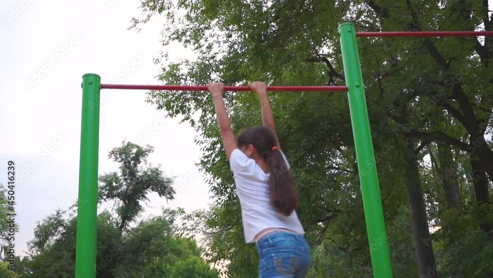 A teenage girl is engaged on horizontal bars. Playground. The child goes in for sports. City block. Leisure park. Workout for health. Competition. A teenage girl is engaged on horizontal bars. Playground. The child goes in for sports. City block. Leisure park. Workout for health. Competition.