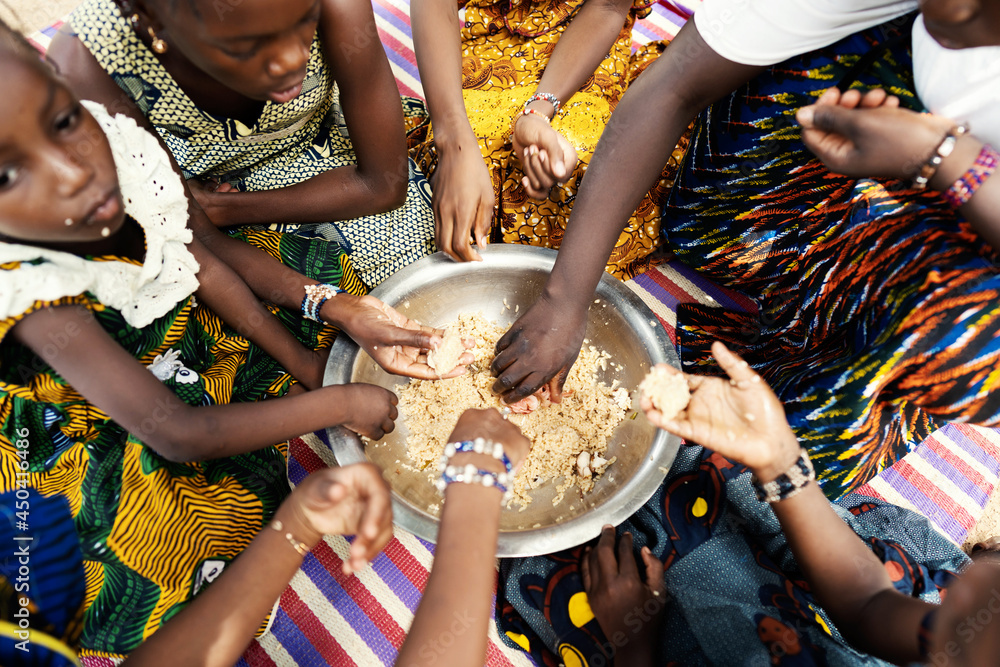 Group of black African girls sitting on a mat, dividing their frugal