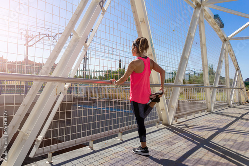 Young woman stretching on a bridge after running while listening to music with headphones. Healthy lifestyle. Selective focus. © Rodrigo