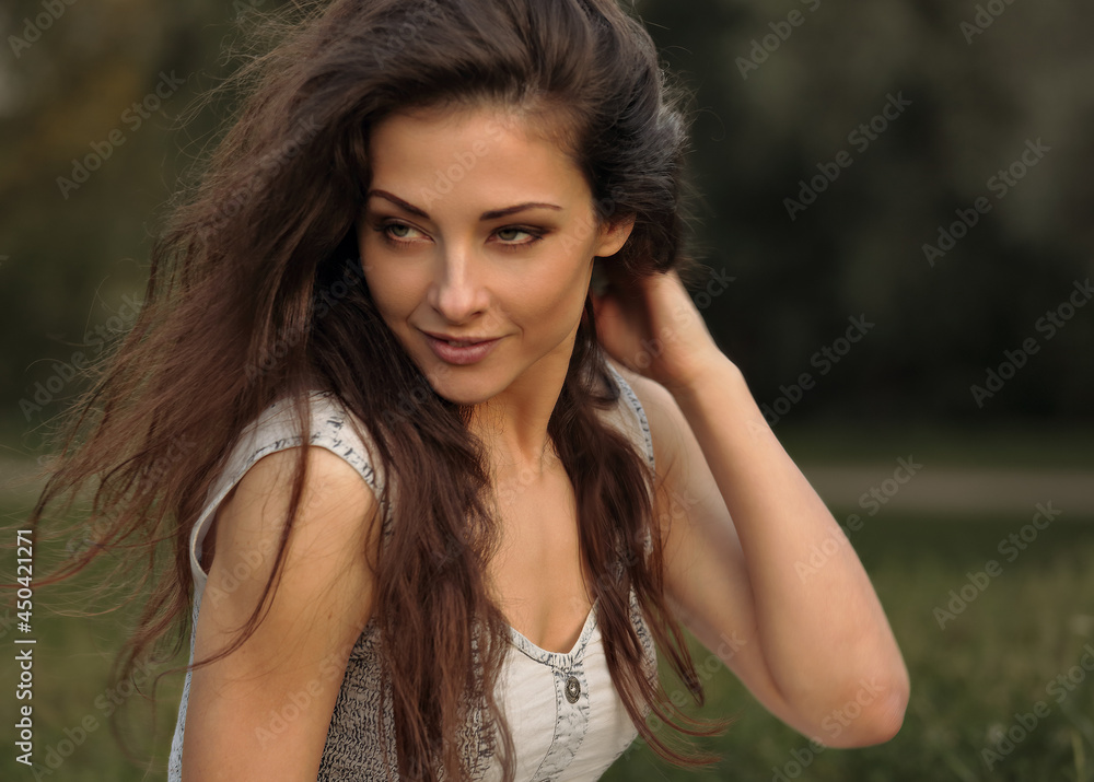 Sexy smiling young woman with long brown hair looking passion on the grass on summer green background. Closeup outdoor bright portrait.