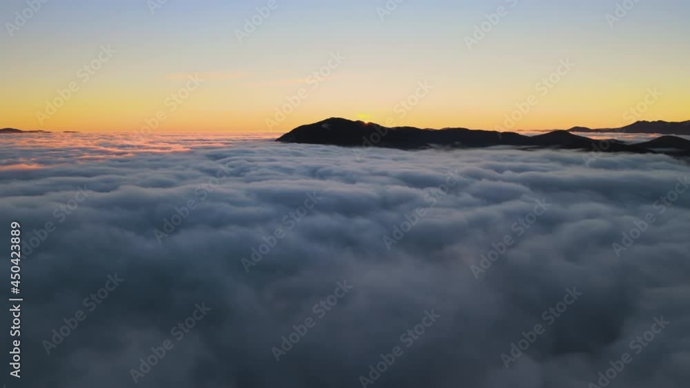 Aerial view of vibrant sunrise over white dense clouds with distant dark mountains on horizon. Aerial view of vibrant sunrise over white dense clouds with distant dark mountains on horizon.