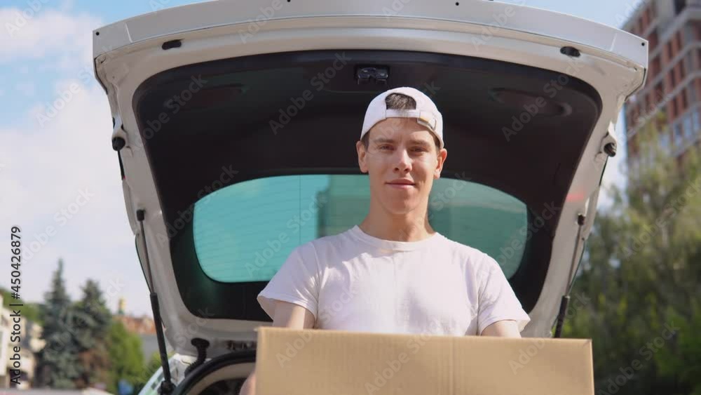 Moving and delivery of manufactured goods. An employee holds a box in his hands and stands next to a car filled with parcels. Express delivery Moving and delivery of manufactured goods. An employee holds a box in his hands and stands next to a car filled with parcels. Express delivery