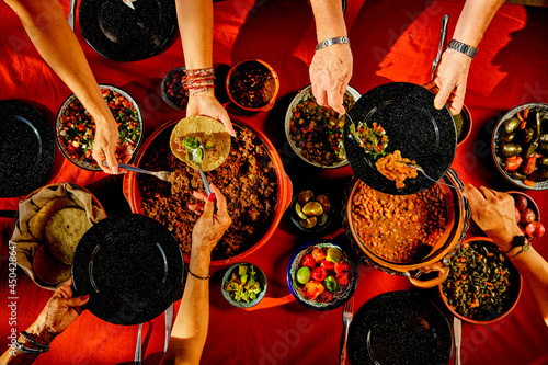Overhead shot of a dinner table with Mexican food and hands. Tacos, beans, carnitas, habanero, salsa