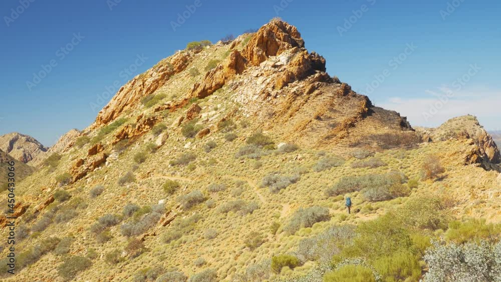 Distant hiker walks across rocky scrub covered peak, Central Australia Distant hiker walks across rocky scrub covered peak, Central Australia