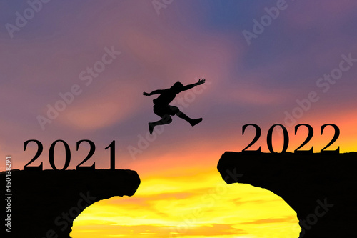 Happy New Year 2022 Men jump over silhouette mountains and sun