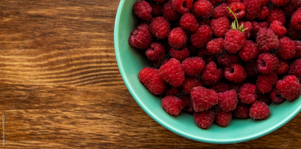 Juicy ripe bright red raspberries in a turquoise deep plate on a wooden background on the right close up Juicy ripe bright red raspberries in a turquoise deep plate on a wooden background on the right close up