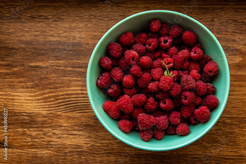 Juicy ripe bright red raspberries in a turquoise deep dish on a wooden background on the right