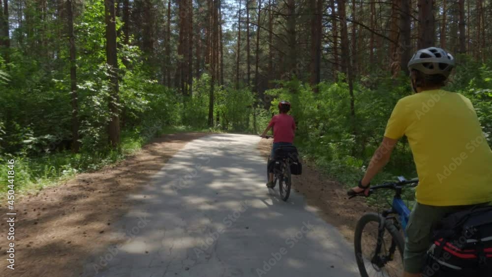 Two travelers are riding bicycles. Young men on bicycles with cycling backpacks ride along a picturesque forest road. Two travelers are riding bicycles. Young men on bicycles with cycling backpacks ride along a picturesque forest road.