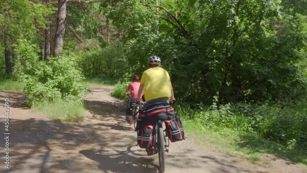 Young people ride bicycles along a forest road. Bicycles are equipped with luggage racks and hiking bags. Young people ride bicycles along a forest road. Bicycles are equipped with luggage racks and hiking bags.