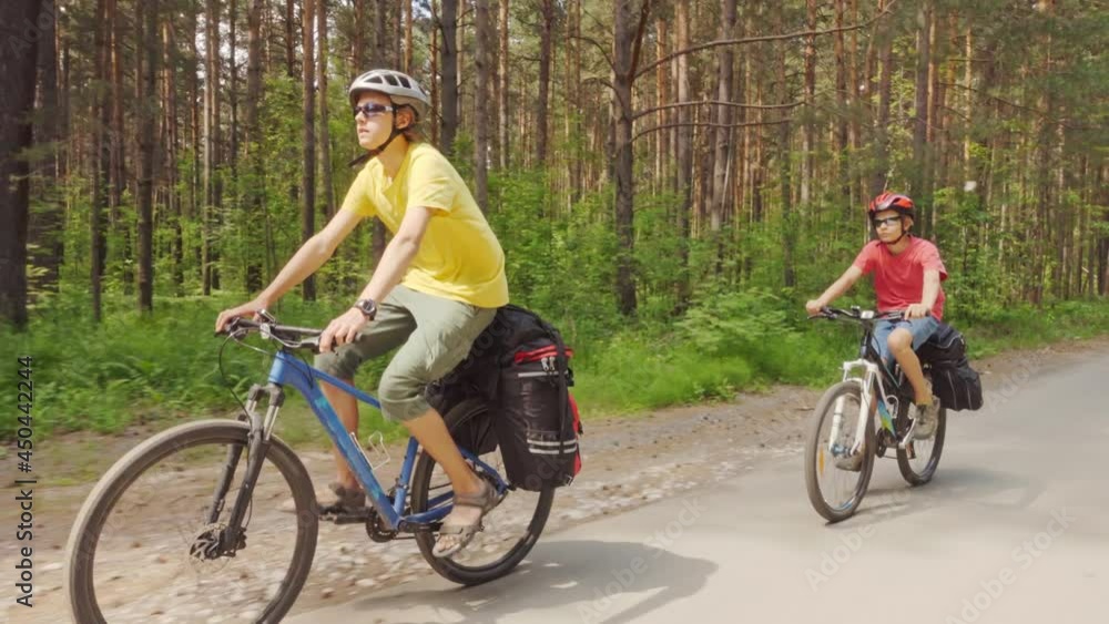 Two young men ride bicycles along a forest road. Cycling trip. Hiking equipment, bicycle backpacks. Two young men ride bicycles along a forest road. Cycling trip. Hiking equipment, bicycle backpacks.
