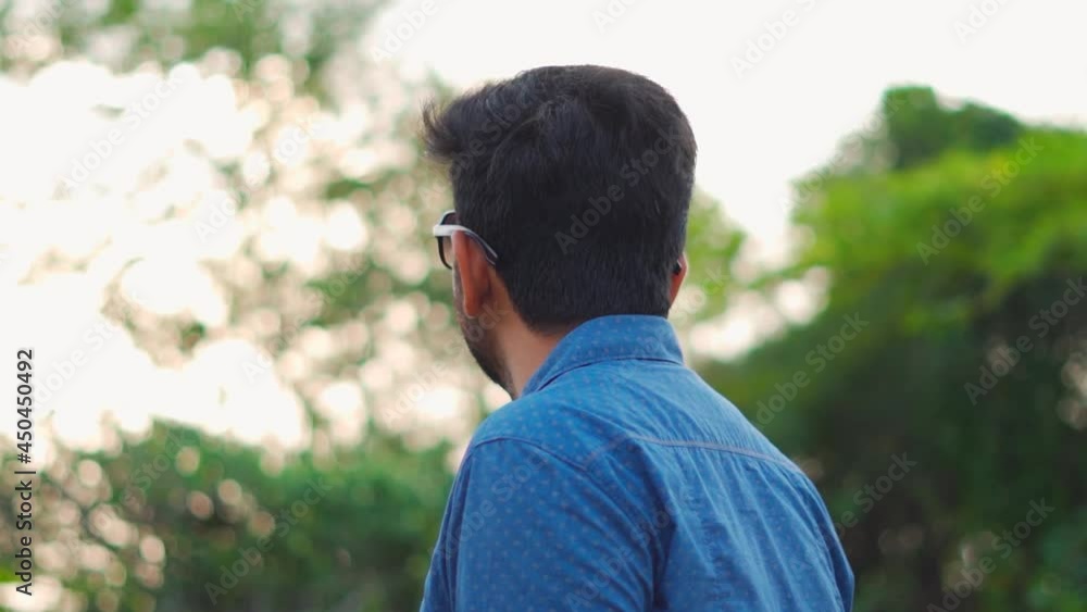 Portrait of an Indian man wearing sunglasses in green park. Cheerful man face with positive emotion outdoors looking at the sky Portrait of an Indian man wearing sunglasses in green park. Cheerful man face with positive emotion outdoors looking at the sky