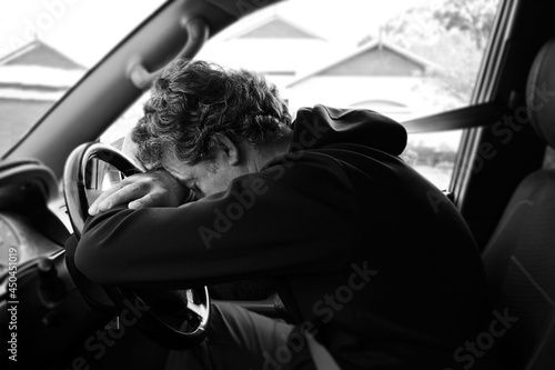Sad and depressed mature adult man sitting in a car leaning on vehicle steering wheel