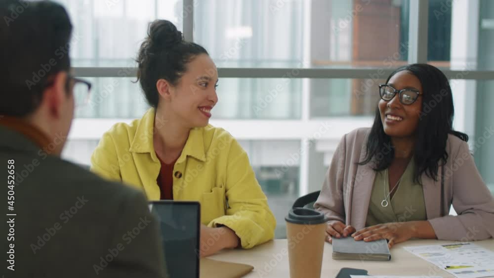 Two multiethnic businesswomen smiling and talking with male colleague during office meeting Two multiethnic businesswomen smiling and talking with male colleague during office meeting