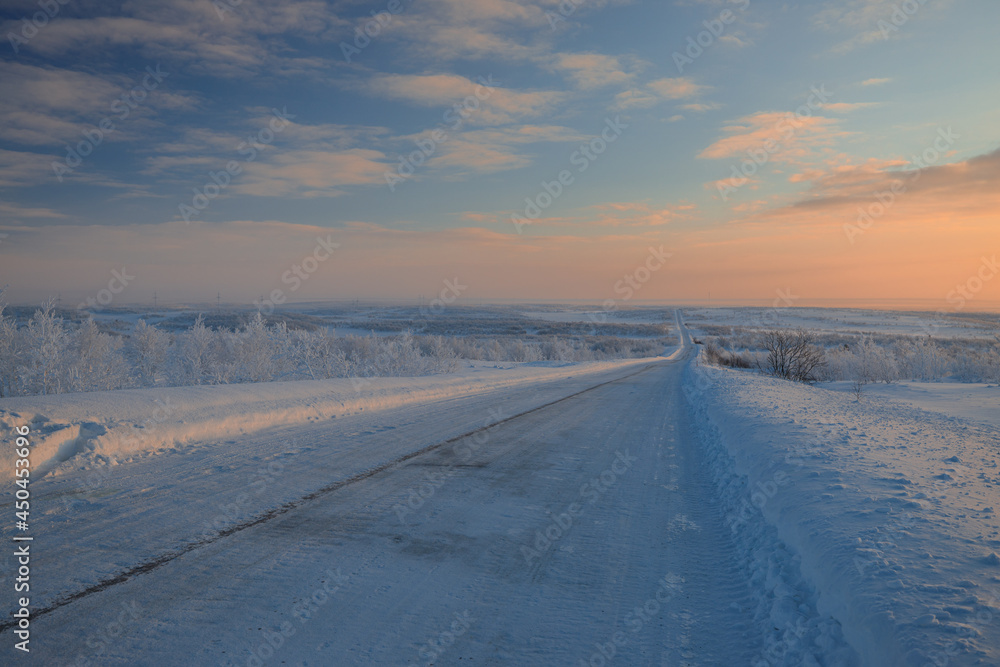 In front of us is a road that goes into the distance at dawn in the middle of a snowy desert. The road to Teriberka