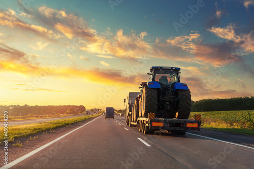 POV heavy industrial truck semi trailer flatbed platform transport two big modern farming tractor machine on common highway road at sunset sunrise sky. Agricultural equipment transportation service photo