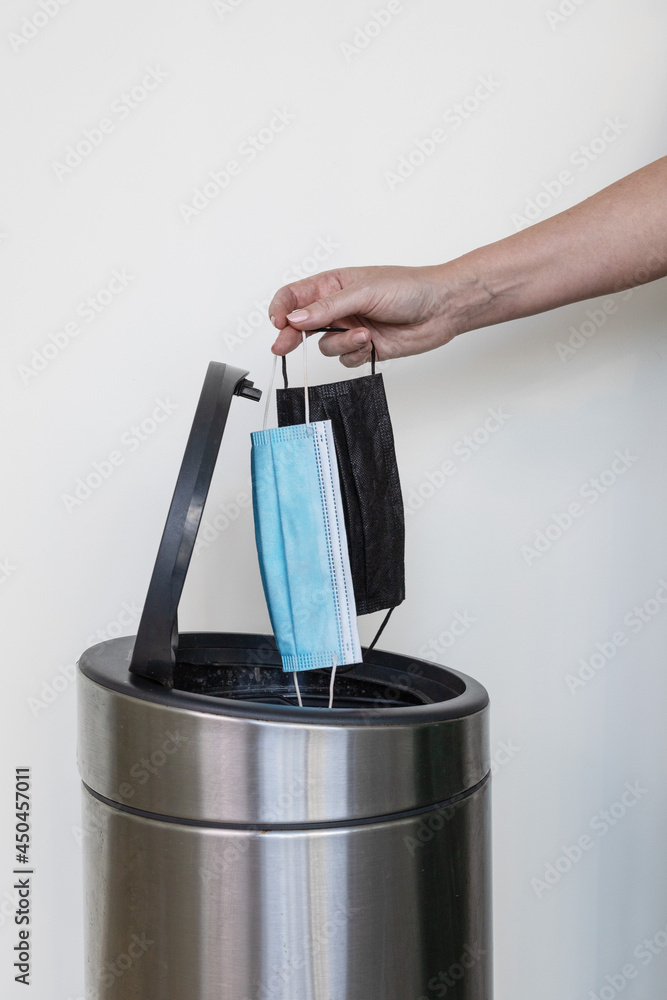 A womans hand throwing out madical face masks in a rubbish bin A womans hand throwing out madical face masks in a rubbish bin