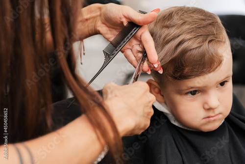 Shooting in a beauty salon. A barber cuts a little boy's hair with scissors