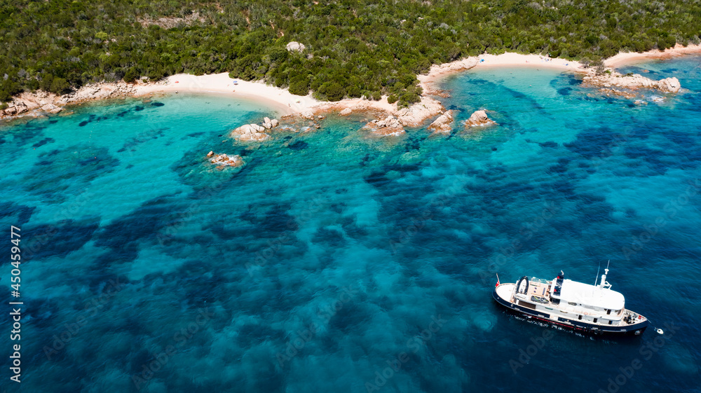 View from above, stunning aerial view of a green coastline with some beautiful beaches and a yacht sailing on a turquoise water. Liscia Ruja, Costa Smeralda, Sardinia, Italy.