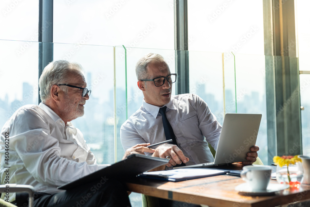 Picture of young business man with his older business partner. They are in white shirt and black tie. They are sitting on a table in a hotel lobby. Picture of young business man with his older business partner. They are in white shirt and black tie. They are sitting on a table in a hotel lobby.