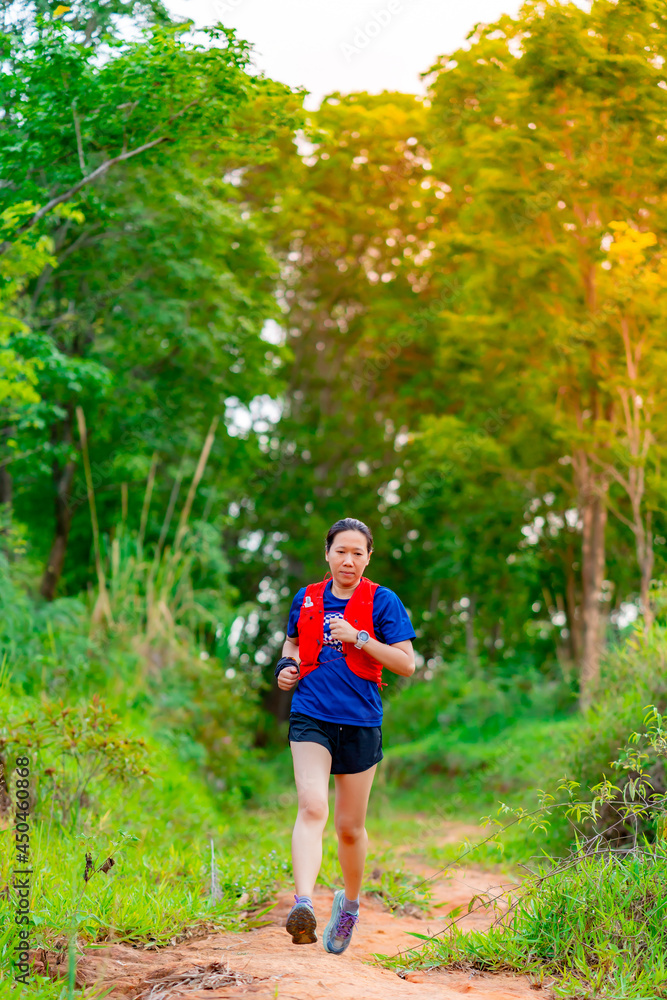 Asian female trail runners, wearing runners, sportswear, practice running on a dirt path in a forest. With a happy mood, there were many green trees in the background. Asian female trail runners, wearing runners, sportswear, practice running on a dirt path in a forest. With a happy mood, there were many green trees in the background.