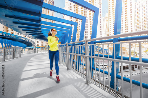 Photography Young woman in bright sportswear quickly runs across a pedestrian bridge in the Dubai Marina district