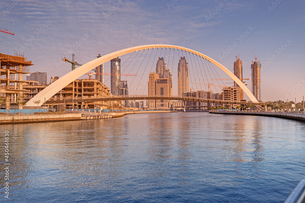 Tolerance bridge and promenade embankment along Dubai Creek Canal with large construction site