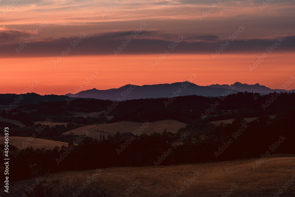 Intense and colored sky during sunset in tuscany, Italy. Mountain silhouettes in the distance, red and orange sky, amazing views of the most famous countryside.