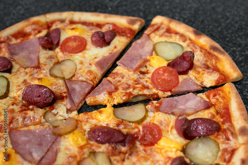 Sliced pizza with sausage  ham  pickles and tomatoes