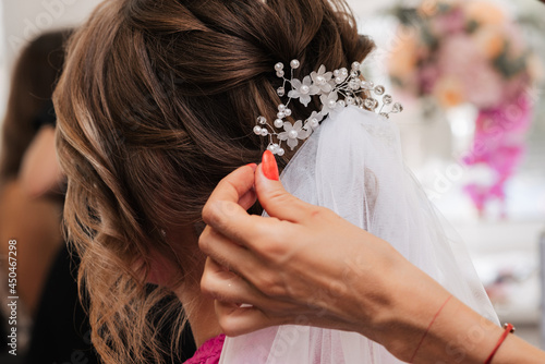 The hairdresser makes an elegant hairstyle for the bride's styling with white jewelry in her hair in the salon