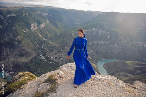 brunette woman in a blue long dress stands on the edge of the Sulak canyon in the evening at sunset in Dagestan