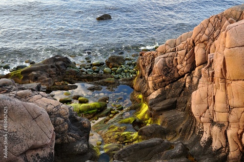 View from the rocks to the sea on large stones of unusual texture in green tones. Landscape over the rocky sea coast. Seascape between stone mountains. The sea from a high mountain on a sunny hot day.