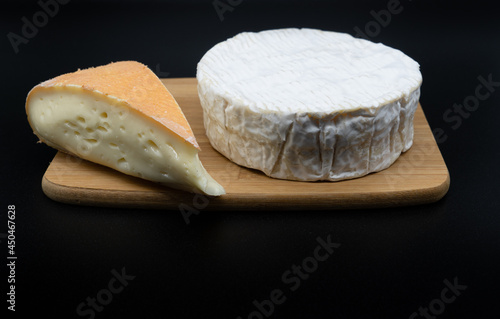 Chaumes and camembert cheese on a cutting board. Two different isolated soft cow's milk cheeses on black background photo