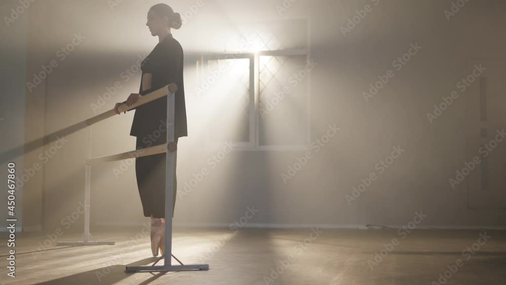Wide shot of confident slim ballerina in pointes walking on tiptoes to barre in backlit fog. Gorgeous Caucasian brunette woman in black suit rehearsing in smoke dance studio Wide shot of confident slim ballerina in pointes walking on tiptoes to barre in backlit fog. Gorgeous Caucasian brunette woman in black suit rehearsing in smoke dance studio