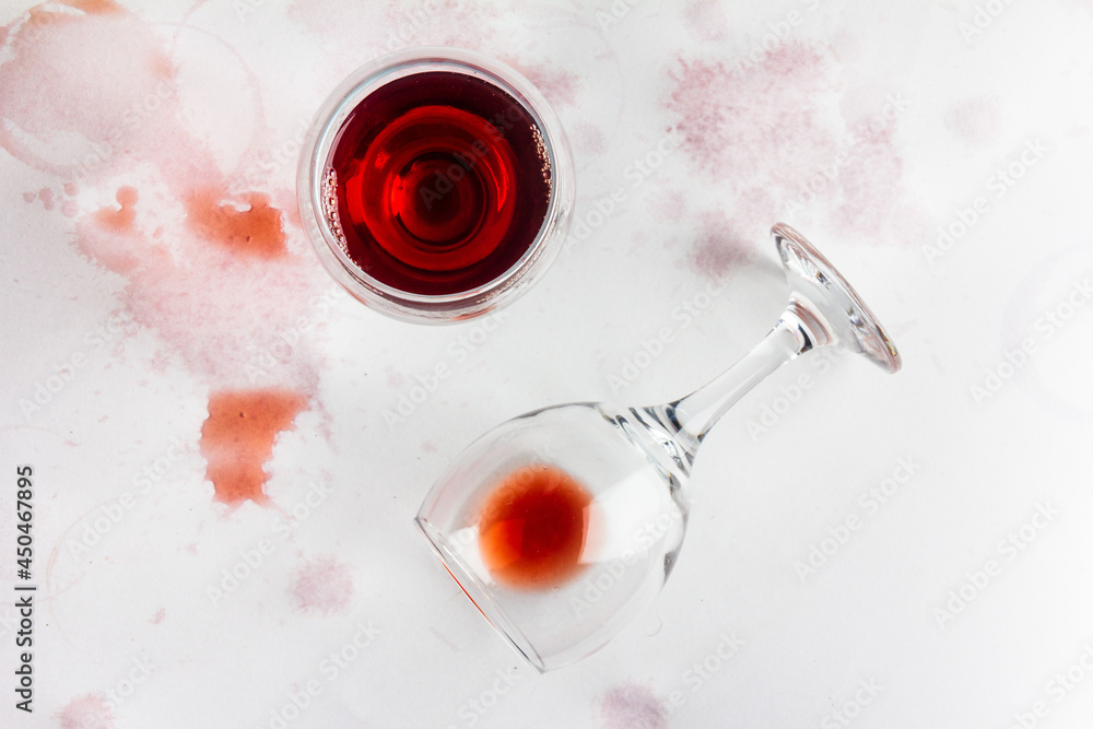 glass of red wine and overturned glass with leftover wine on a white background, drenched and stained with wine, top view glass of red wine and overturned glass with leftover wine on a white background, drenched and stained with wine, top view