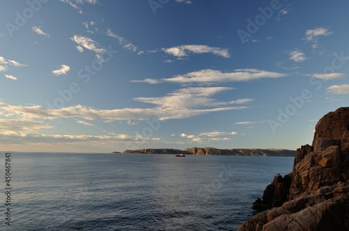 Nice view of the sea and the sailing ship in the distance. Beautiful textured rocks, mountains and blue sea backgrounds. Dark sea water and blue sky with small clouds. Hot day in the mountains.