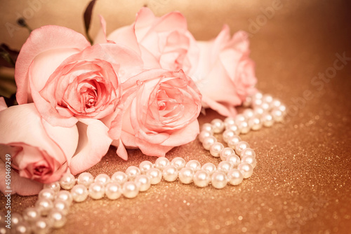 Pink rose and pearl necklace on a shiny gold background
