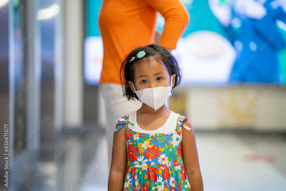 Cute small girl wearing protective face mask standing in shopping mall.