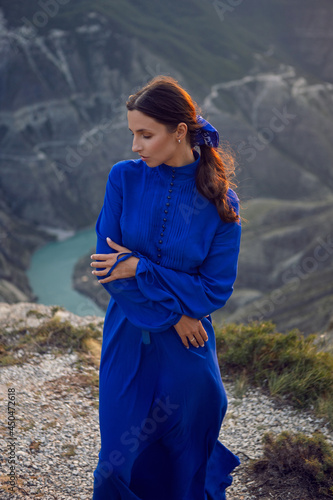 brunette woman in a blue long dress stands on the edge of the Sulak canyon in the evening at sunset in Dagestan