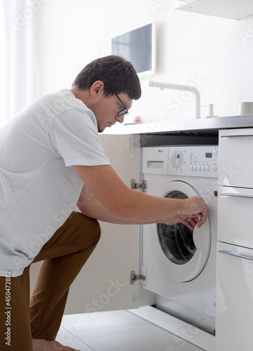 Young man putting clothes into washing machine