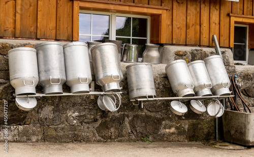 große Milchkannen vor einer Berghütte zum Trocknen auf Gestänge kopfüber gestellt.