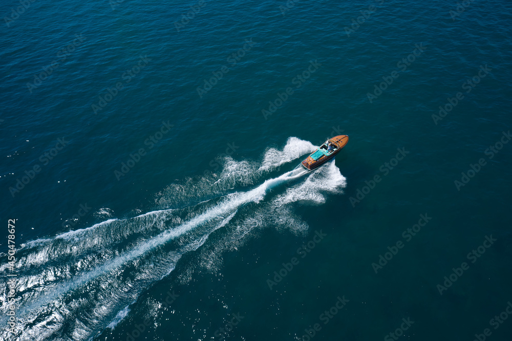 Obraz premium Classic Italian wooden boat fast moving aerial view. Top view of a wooden open large motor boat. Luxurious wooden boat fast movement on dark water.