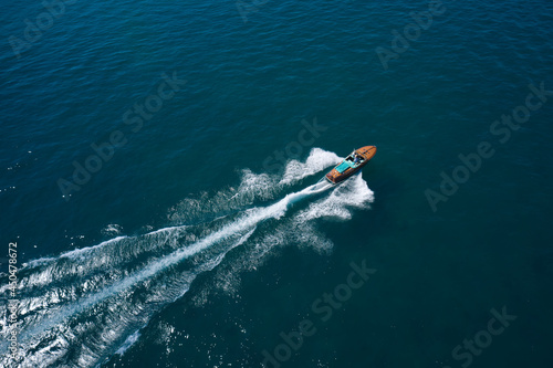 Classic Italian wooden boat fast moving aerial view. Top view of a wooden open large motor boat. Luxurious wooden boat fast movement on dark water.