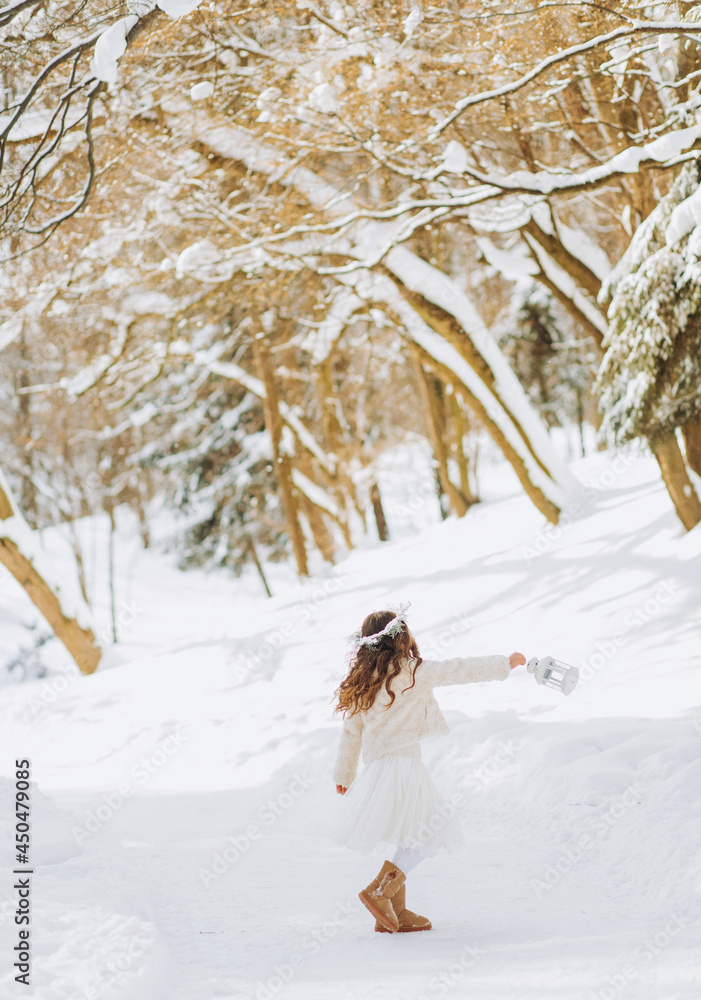 Happy little girl runs on a forest path with a lantern in her hand. Christmas time. Sunny winter day.